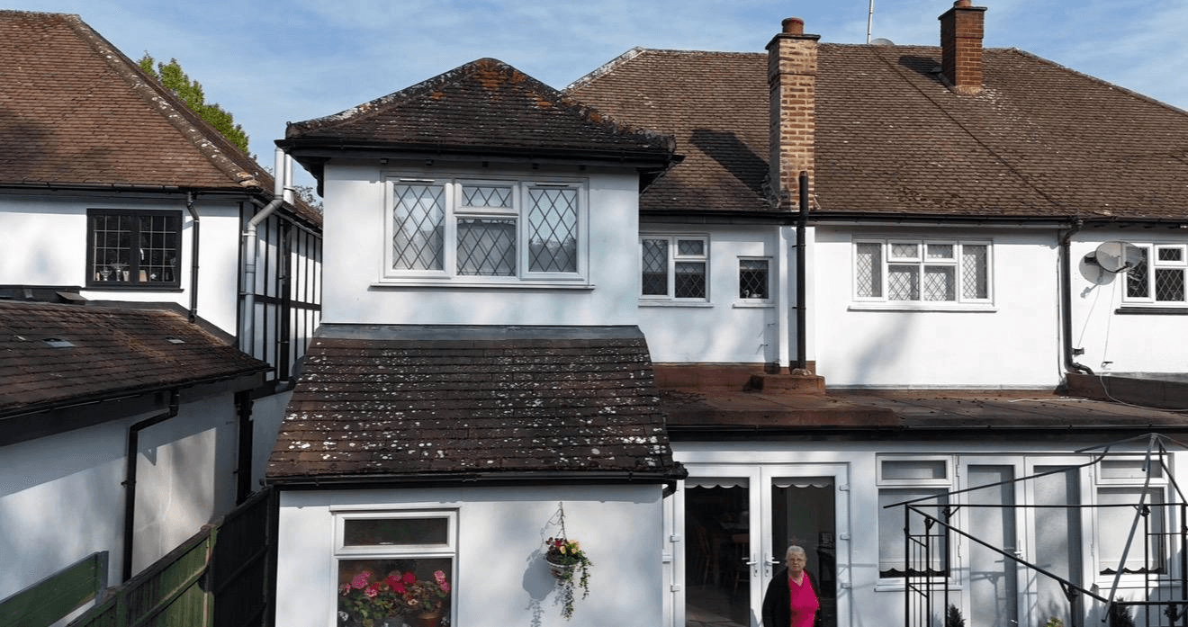 Semi-detached house with grimy dark moss-covered roof tiles before cleaning